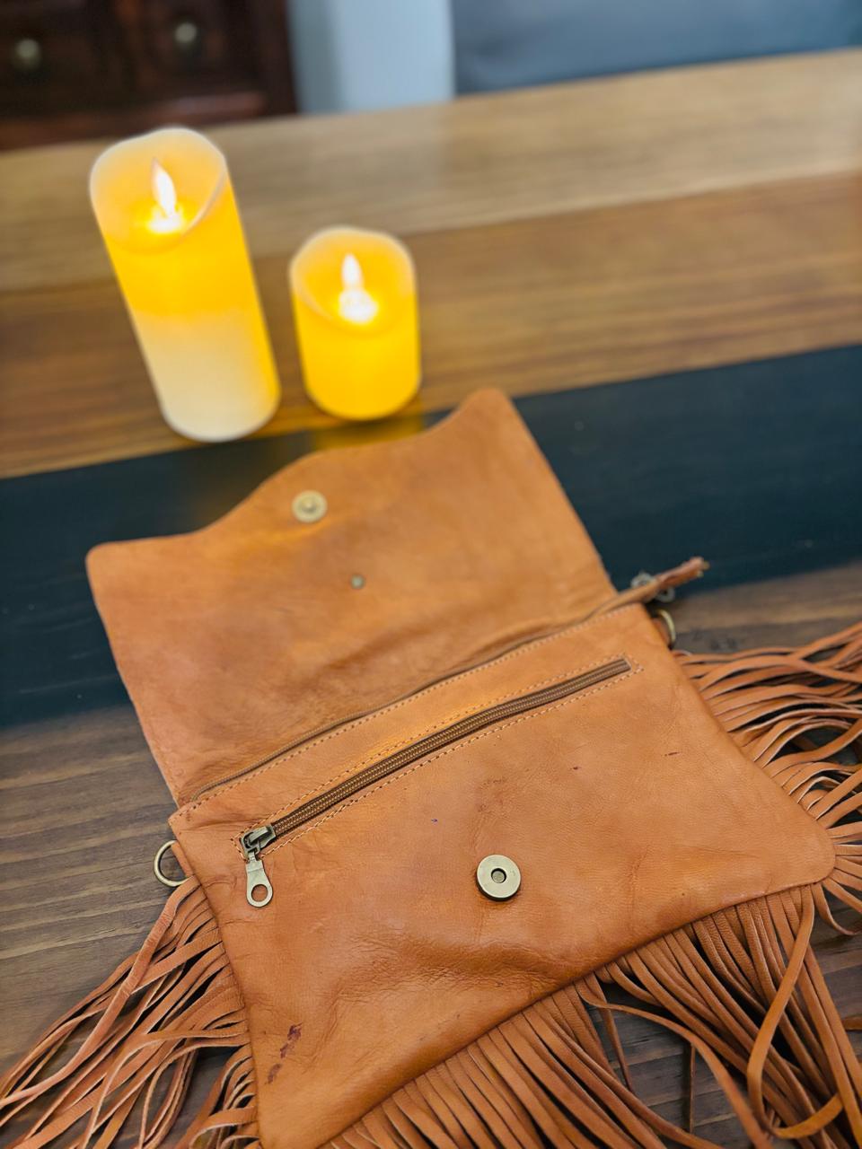 Atlas Maple Nomad Fringe Crossbody bag with leather strap and decorative fringe detailing, shown in a natural outdoor setting.